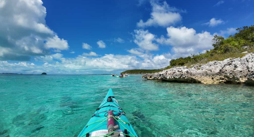 From inside a blue kayak clear blue water stretches out under blue skies dotted with clouds